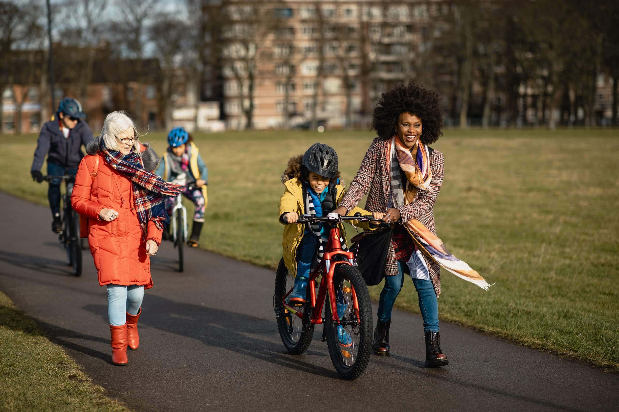 Women holding onto a child's bike laughing through a park as another women looks on smiling.