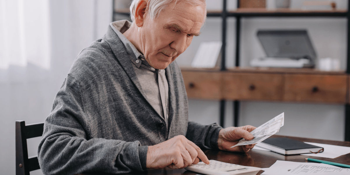 Senior Man Sitting at table with paperwork and using calculator while counting money