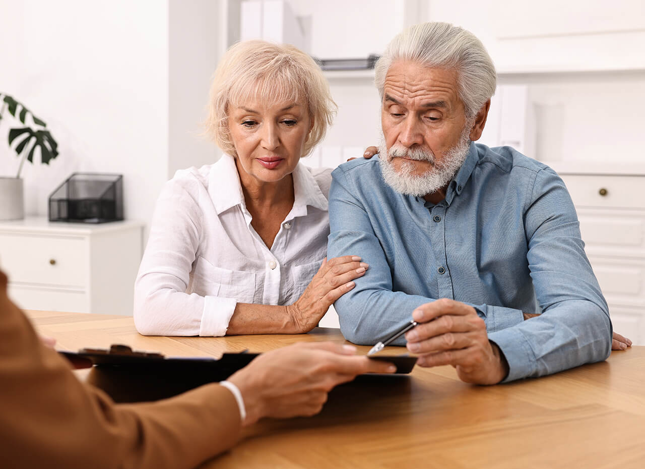 Senior couple consulting with a specialist at wooden table indoors.