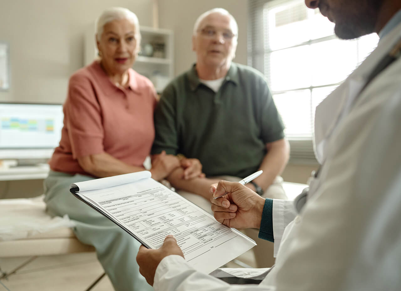 Senior couple consulting doctor in clinic, reviewing medical form and discussing treatment plan.