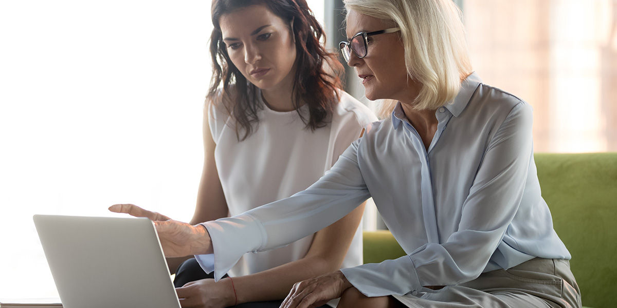 Serious middle aged executive manager explaining to client online work together pointing at laptop.