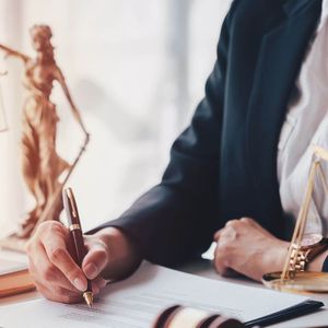 Lawyer Signing Legal Documents in Office with Lady Justice Statue Scales of Justice